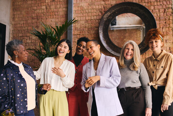 Portrait of cheerful multiethnic businesswomen laughing and smiling in office with exposed brick...