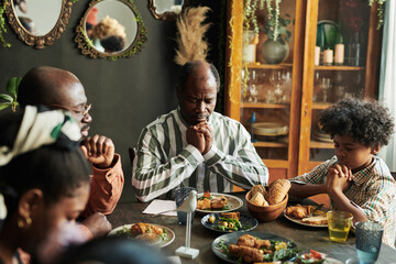 African family sitting at dining table with eyes closed and praying together before dinner