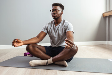 Mid adult man practicing yoga in lotus position. Full length of male is exercising on hardwood...