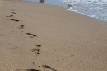 Footprints in the sand beach. Footprints in the sand against a sea wave. Footprints on a sunny day with golden sand, beach, wave and footsteps