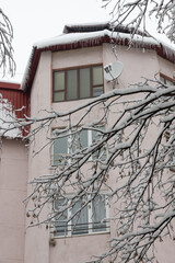 Facade of a residential building in the suburbs during a snowfall. The wall of the house and the balcony are covered with snow. Tree branches covered with snow on a cold winter day
