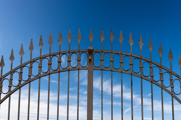 Close-up of a wrought iron gate with sharp points on blue sky with clouds and copy space.