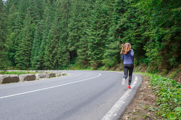 Runner woman running on the mountain road through the forest.