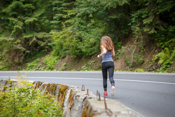 Young fitness woman running on the road through the forest