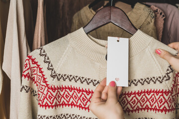 Woman customer looking on tag choosing sweater with christmas ornament in garment store. Shopping. Winter. Copy space