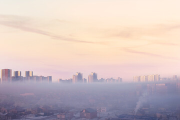 Winter, snow town buildings, skyscrapers on horizon. Village at early morning fog and pink pastel sky at sunrise