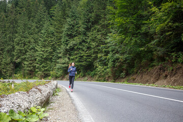 Obraz premium Runner woman running on the mountain road through the forest.