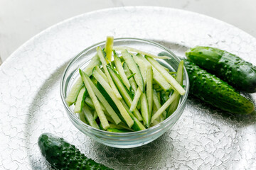 Cucumbers cut into strips in a glass cup on a silver tray.
