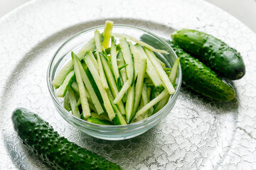 Cucumbers cut into strips in a glass cup on a silver tray.