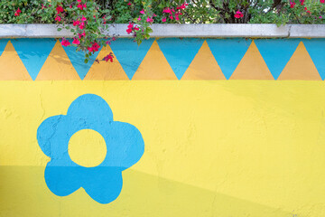 Yellow wall with a single blue painted flower. At the top there is an orange triangular border and...