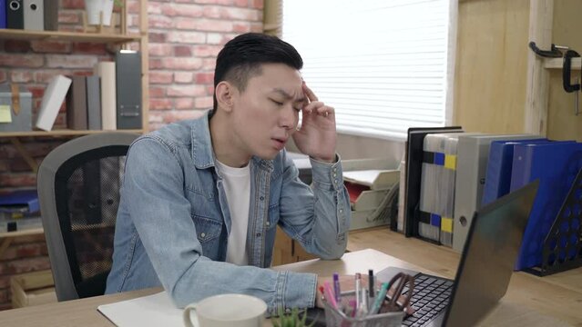 asian young male is propping his head and staring at the monitor while pondering on a difficult project on the computer in the office.
