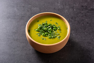 Green pea soup in a wooden bowl on black background