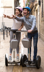 Fototapeta na wymiar young couple guy and girl walking on segway in streets of european city