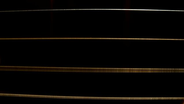 Macro Shot Of Acoustic Guitar Strings On Black Background. The Strings Vibrate To Reproduce The Melody Of The Song. Vibrating Guitar Strings Close Up. Stringed Musical Instrument That Plays A Melody.