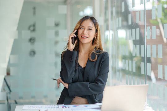 Beautiful young Asian business woman charming smiling and talking on the mobile phone in the office.