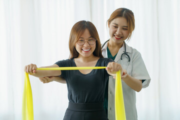 Asian woman physiotherapist oversees the patient’s stretching with elastic tape.