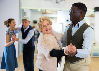 Elderly woman learning ballroom dancing in pair in dance studio