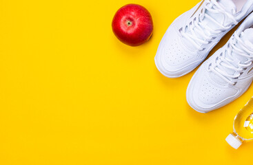 Fototapeta na wymiar On a bright yellow background, a pair of white sneakers, a bottle of water and a red apple. The concept of a healthy lifestyle. Copy space