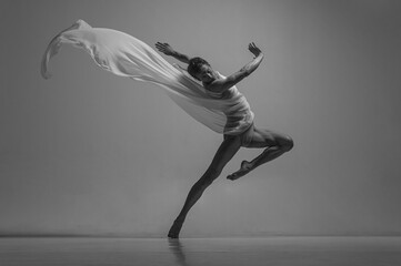 Hope. Black and white portrait of graceful muscled male ballet dancer dancing with fabric, cloth...
