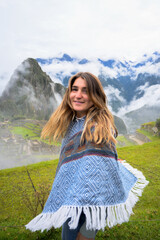Portrait of a caucasian woman smiling and wearing the typical peruvian poncho in front of Machu Picchu inca city. - obrazy, fototapety, plakaty