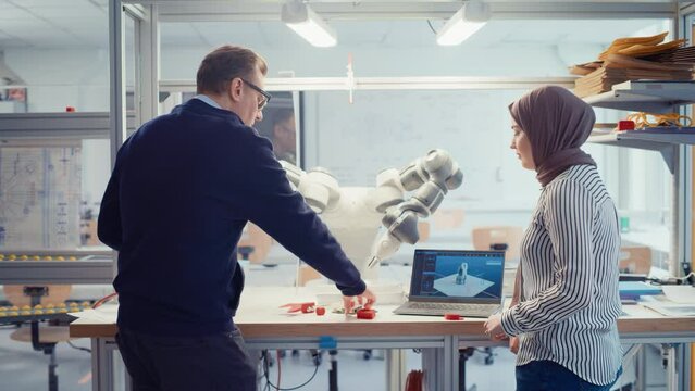 Chief Male Engineer Chatting with Arabic Female Computer Science Specialist While Gathering at the Table with Robotic Hand. Promising Computer Scientist Collaboration Concept. Medium Shot