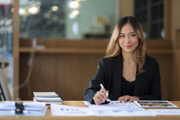 Fototapeta premium Portrait of a business woman working or secretary with laptop and financial documents on the desk in the office. Looking at camera.
