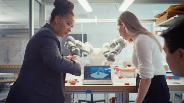 Brilliant Future Students and Black Senior Engineer Use Programmable Robot Hand and Manipulate it with Laptop. High Tech Research Laboratory with Modern Equipment. Zoom Out Shot