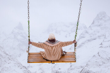A girl swings in winter on a swing high in the mountains