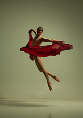 One young muscled man, flexible ballet dancer in action with red fabric, cloth isolated on olive...
