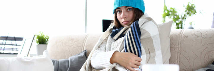 Young sad sick woman wearing hat and blanket
