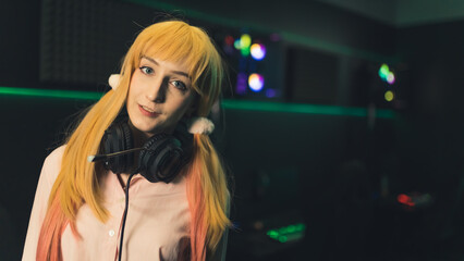 Medium closeup portrait of cute competitive caucasian gamer girl in headset looking at camera. Internet cafe or professional studio in the background. High quality photo