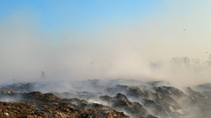 Burning pile of garbage at dump ground or landfill releasing toxic smoke in environment and polluting air	