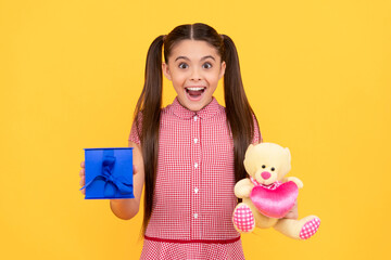 surprised kid hold bear toy and gift box on yellow background, childrens day