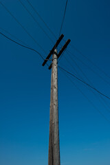 Old wooden pole and wires for communication against the blue sky.