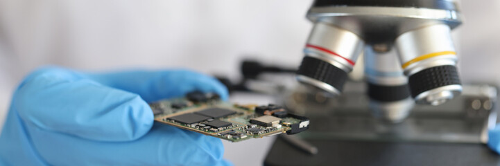 Fototapeta na wymiar Engineer in glove holds microcircuit against background of microscope