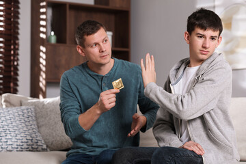 Father talking with his teenage son about contraception at home. Sex education concept