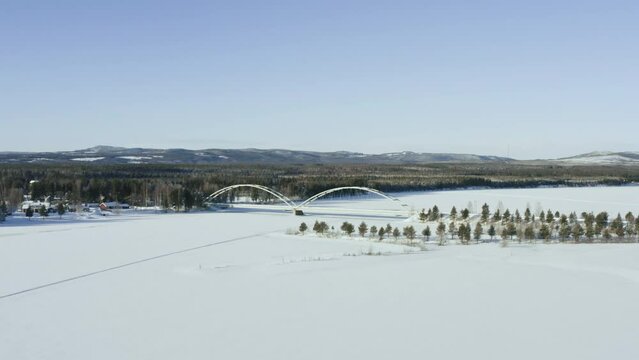 Aerial view of a bridge over a river in the woods in winter. Beautiful urban landscape with snow covered trees and lake.