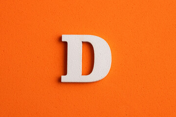 White wooden capital letter D on orange foamy background