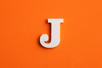 White wooden capital letter J on orange foamy background