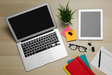 Fototapeta premium Modern gadgets, glasses and office stationery on wooden table, flat lay. Distance learning