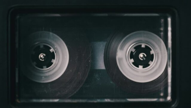 Audio cassette playing in a deck of an old tape recorder. Vintage transparent audiocassette with blank label in retro player spinning. Close-up. Call recording, retro playback, reel with tape rotating