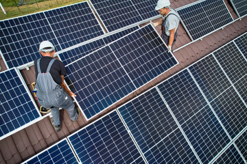 Men technicians mounting photovoltaic solar moduls on roof of house. Electricians in helmets...