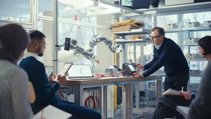 Diverse Computer Specialists Listen and Write while Senior Engineer Change Position of Robot Arm with Controller. Intellectual Educational Environment Concept