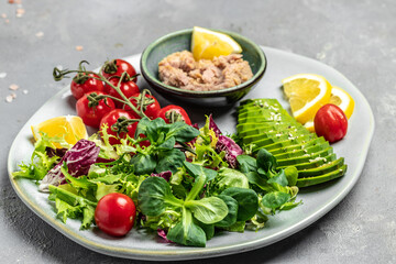Tuna fish salad on light background. Lettuce, cherry tomatoes, avocado and red onions. Clean healthy detox eating. Vegan vegetarian food. Making healthy salad. top view
