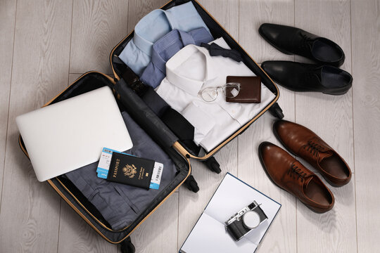 Open suitcase with men's clothes, accessories and shoes on floor, flat lay