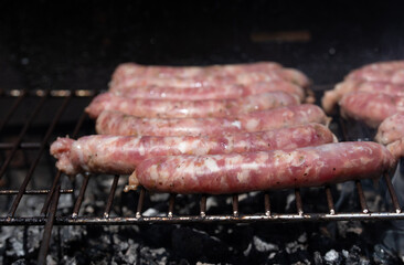 Raw fresh fried sausages, traditional Italian 'salsiccia' lie on a rustic grill over hot charcoal