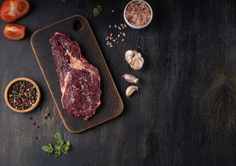 Raw fresh meat Ribeye Steak, seasoning and fresh tomato on wooden background. Copy space