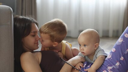 happy mother and two baby toddler children lying on floor, playing together. little son kissing mother in nose, mom smiling. parenthood motherhood concept. happy family lifestyle. - Powered by Adobe