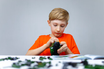 the boy is playing with a plastic constructor, he is attaching the detail of the constructor