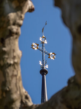 Cross on a church in Murten, Switzerland, photographed through tree branches